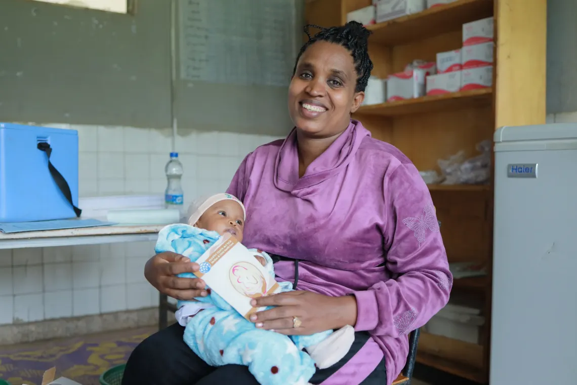 A mother holding her baby in her hand and showing her baby's vaccine card
