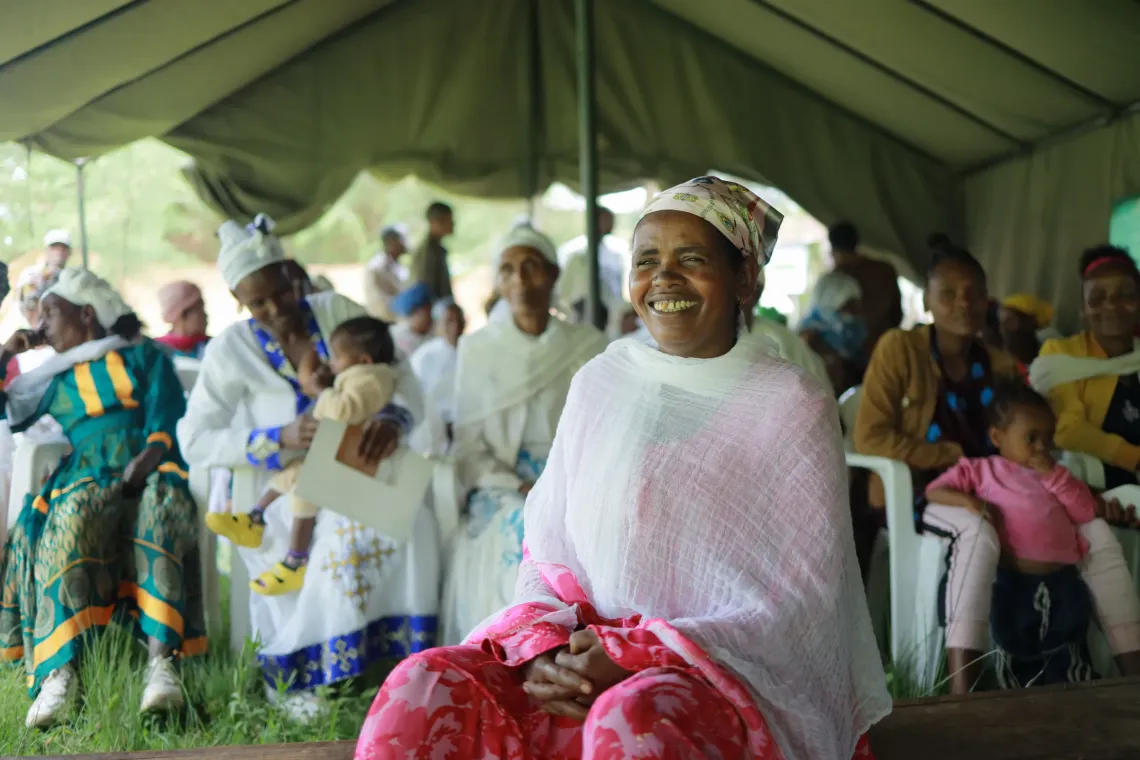 A mother sitting Infront of a community gathering and smiling for the camera