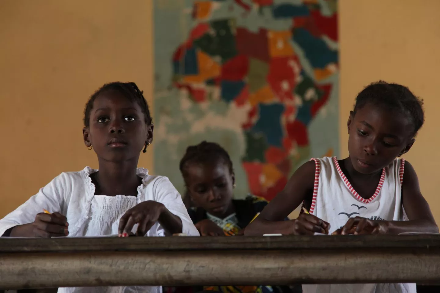 Girls attend a Grade 3 class in a school in the town of Buba, capital of Quinara Region. A map of Africa is on the wall behind them. UNICEF provides notebooks and benches, and supports latrines, handpumps and hand-washing facilities at the school.