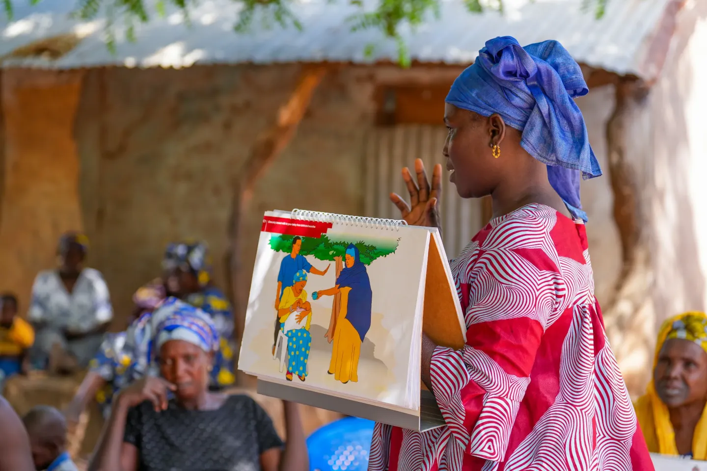 Halima Mbye leads a community session on exclusive breastfeeding in Cheken, North Bank Region. The counselling card (Health and Nutrition flipchart) reminds families to give only breast milk for the first six months.