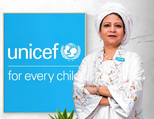 UNICEF Gambia Representative pose for a photo in front of a framed UNICEF logo