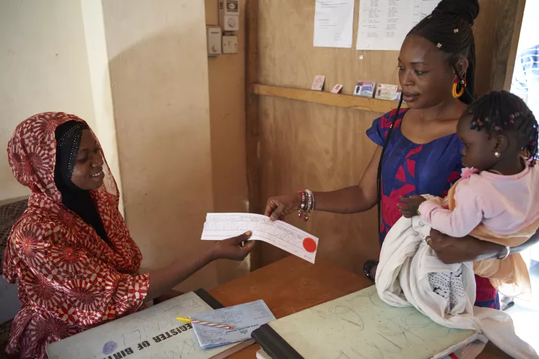 A public health worker hands over a birth certificate to a mother