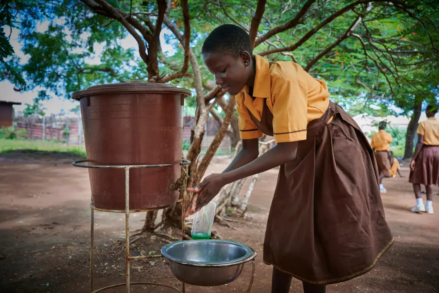 A young girl washes her hands near a water tank outside her classroom.