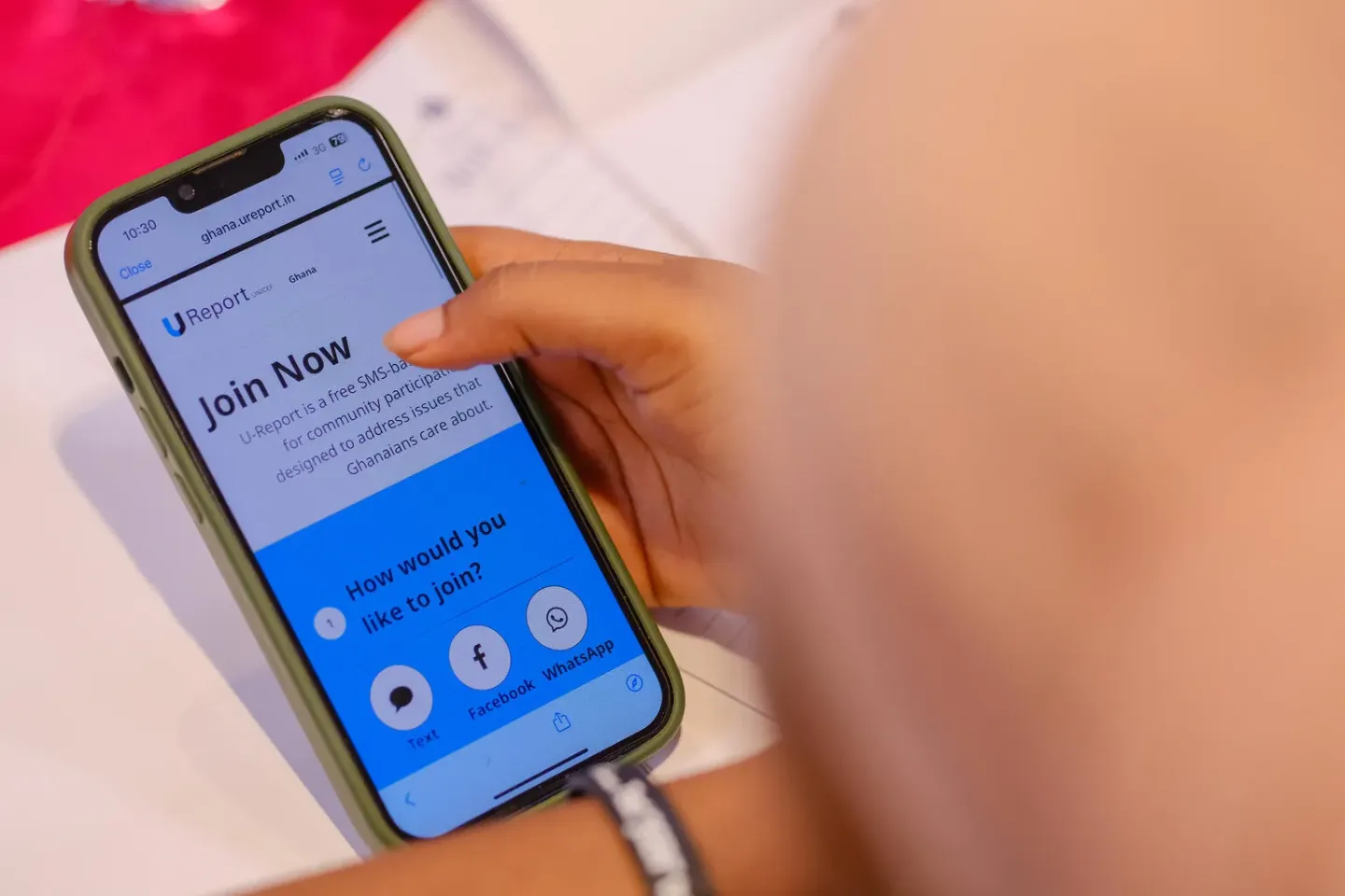 A hand holding a smartphone displaying the U-Report web screen with three circular action buttons.