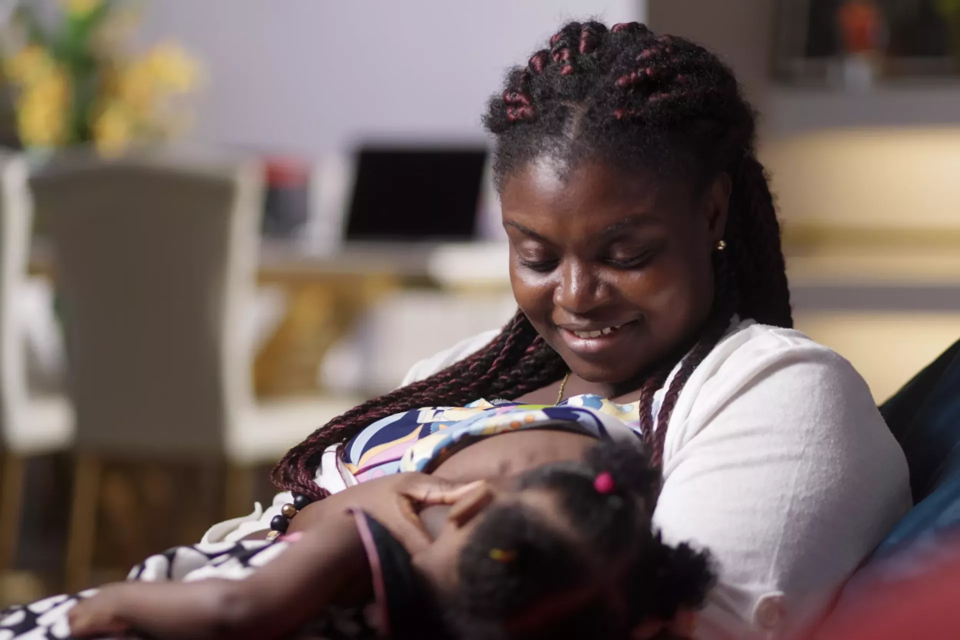 A woman breastfeeds her baby while sitting down on a couch with eye-to-eye contact with the baby..