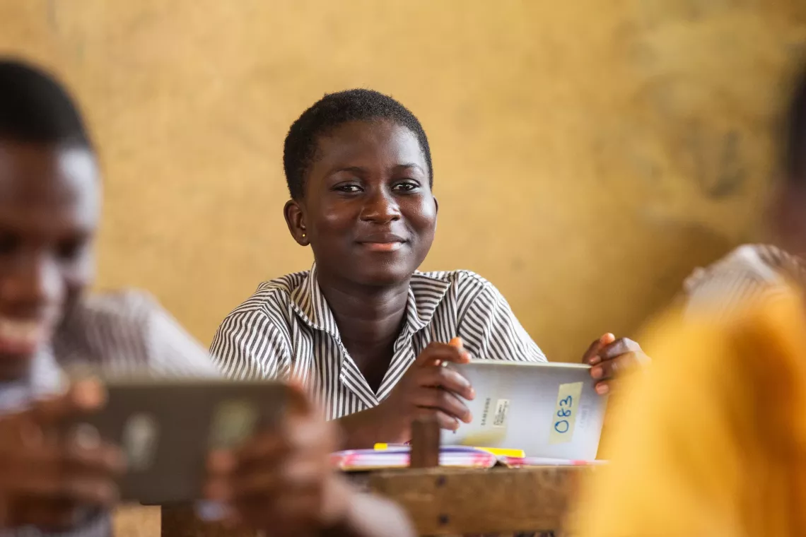 A girl in a classroom holds a tablet with a smile.