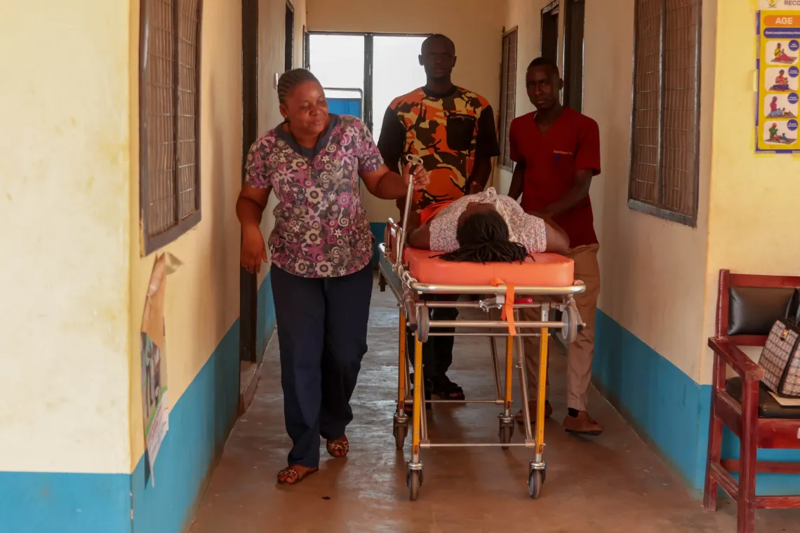 Health workers and community volunteers move a pregnant woman onto a stretcher for referral to a higher-level health facility. 