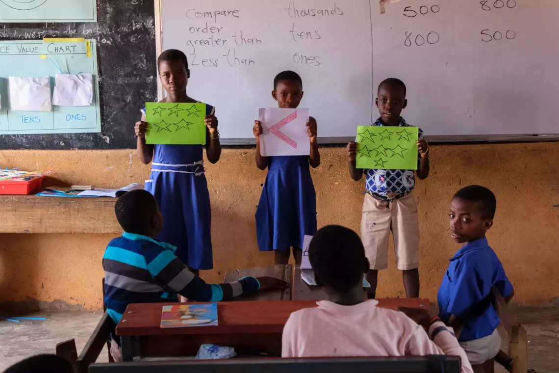 Children hold paper cards in front of their peers in class to illustrate a solution to a math problem.