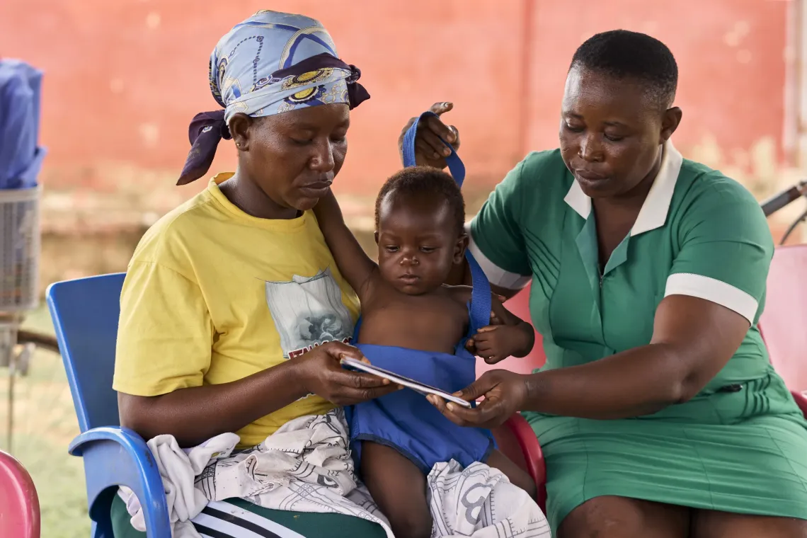 A female health worker hands over the maternal record book to a mother as the watches on.