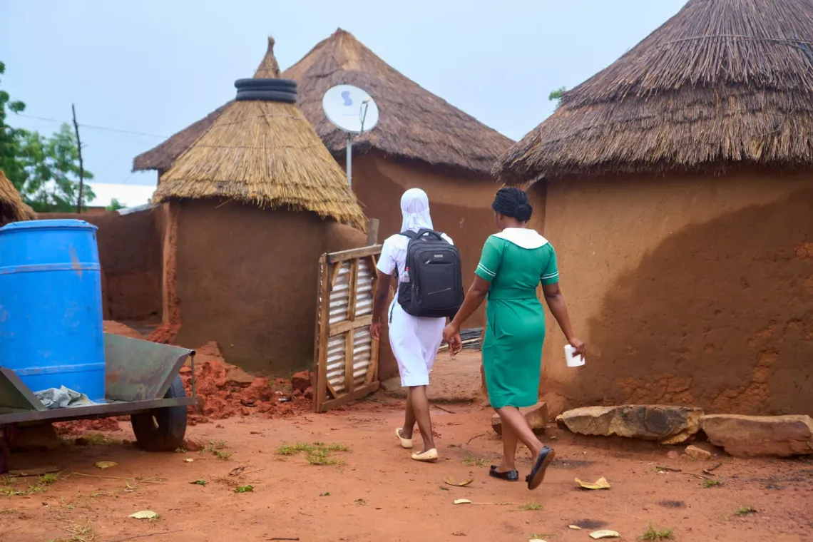 In Nagboo, North East Ghana, nurse Fouzia and her colleague walk through traditional huts to visit a new mother - symbolising the reach of UNICEF‑supported community health care that brings vital guidance and follow‑up directly to families in rural areas.