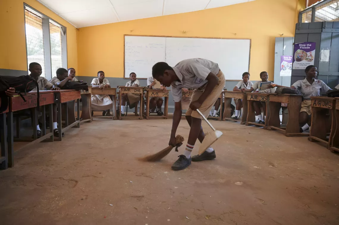 Students watches as a male student sweeps the class. 
