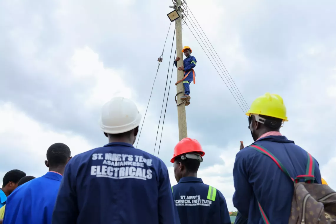 young students watches as ntheir colleague works on a street pole 