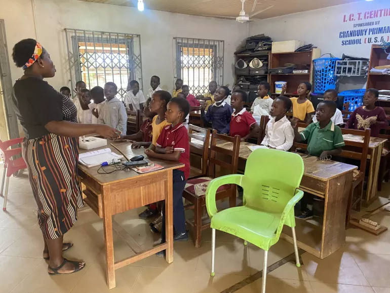 Liberty Manu is teaching her class while her students stand up to participate in an activity. 