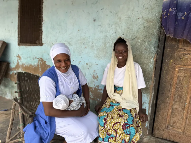 Health workers hold a baby in their arms whilst the mother sits and engages with her.