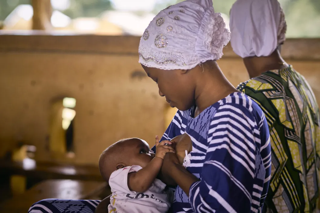 Mother breastfeeds her child as the child stares at her.