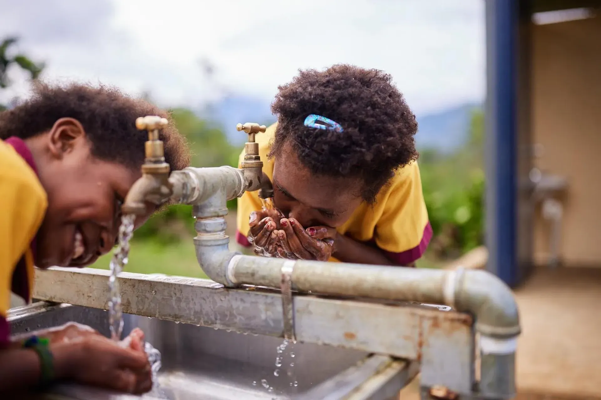 Two girls drinking water from the tap.