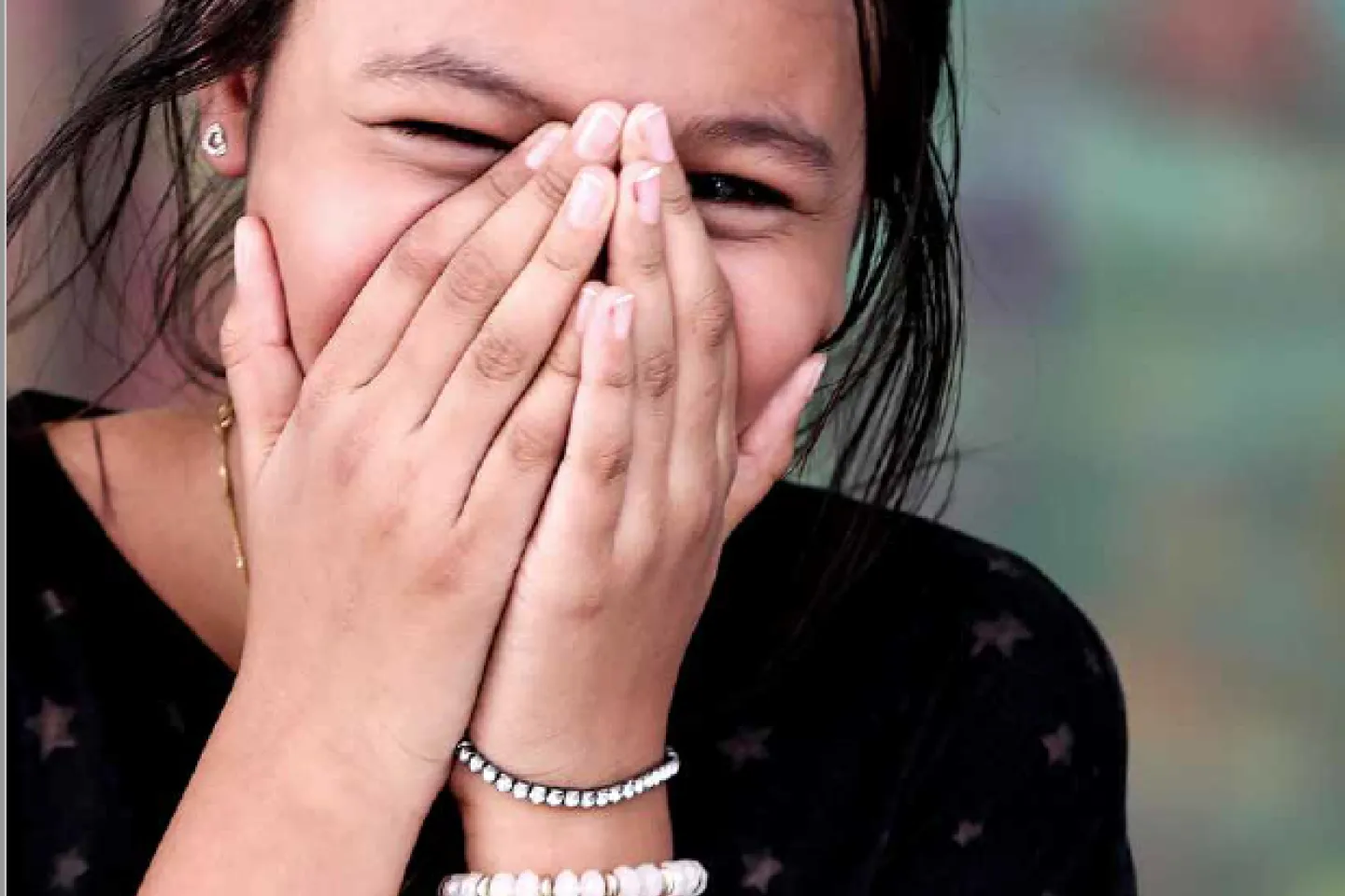 A smiling girl covering her face with her hands.