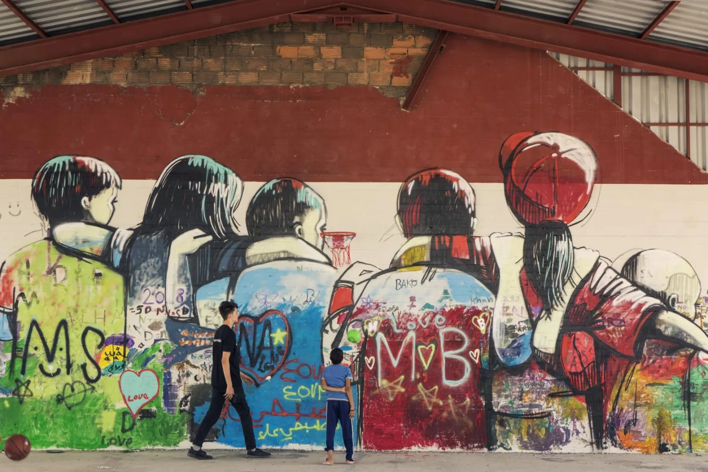 Two children standing and looking at a large mural of children painted on a wall