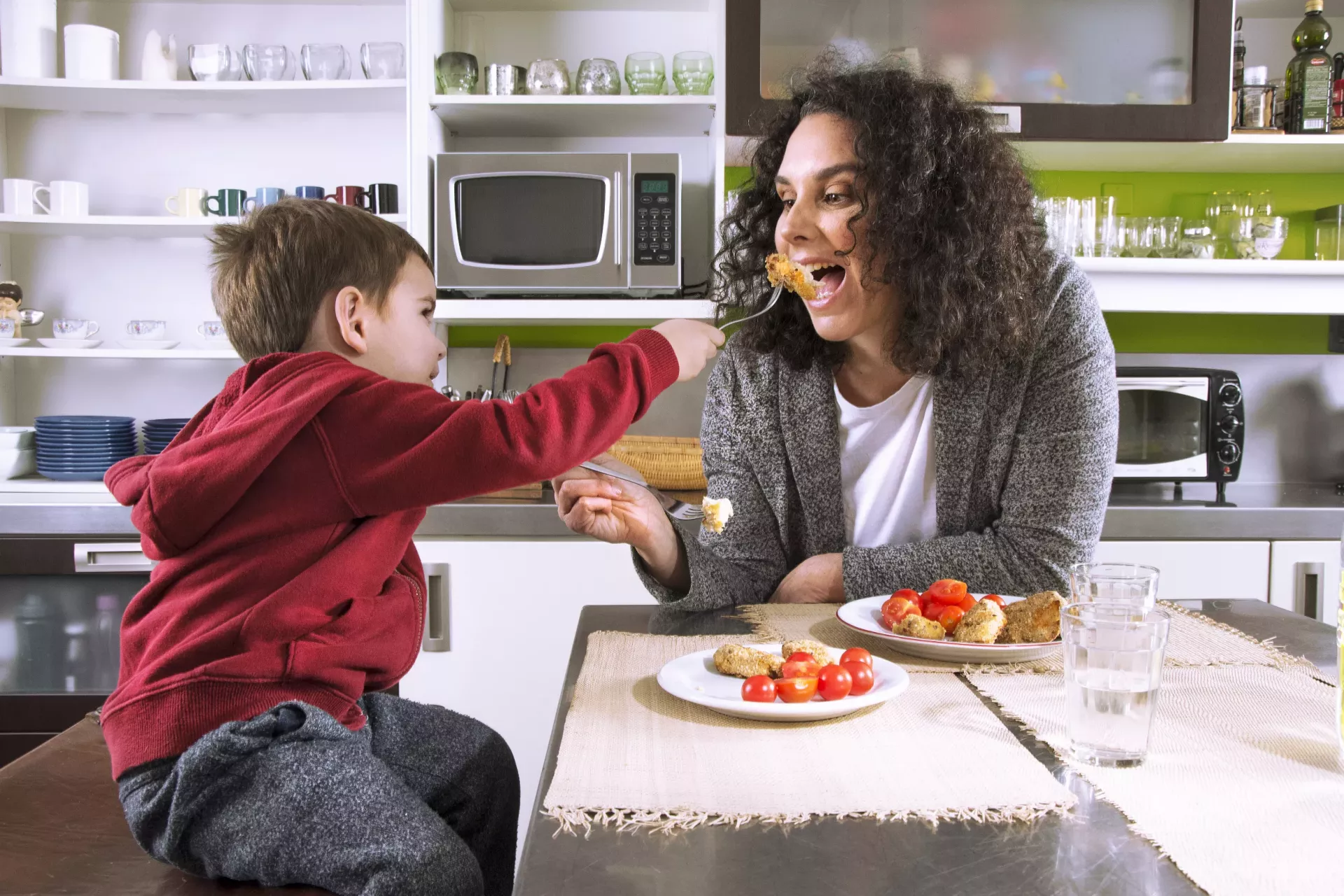 A little boy on kitcen table feeding his mom.