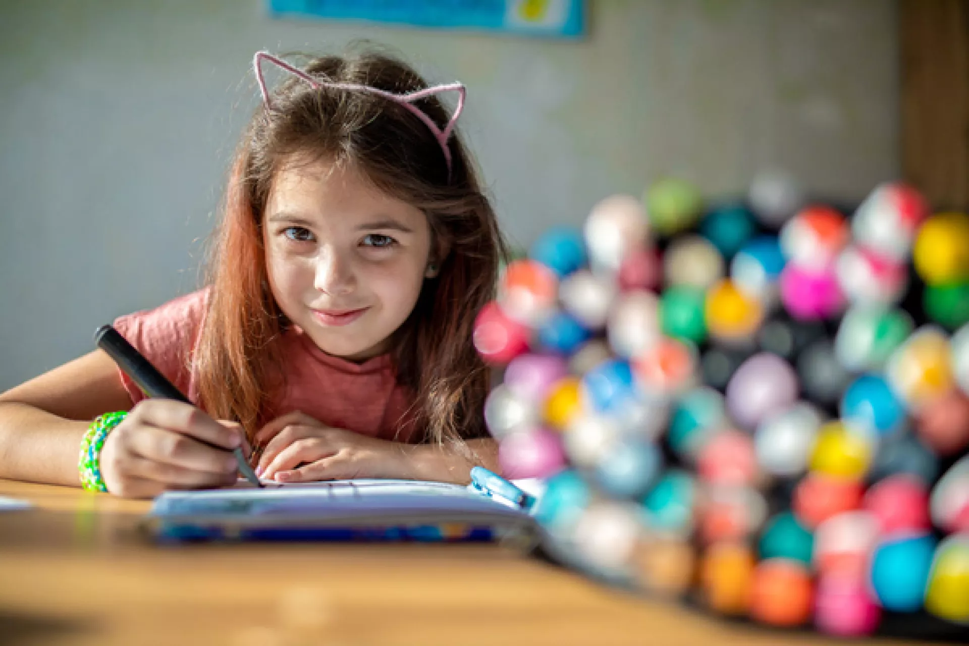 A young smiling girl drawing on a notebook.