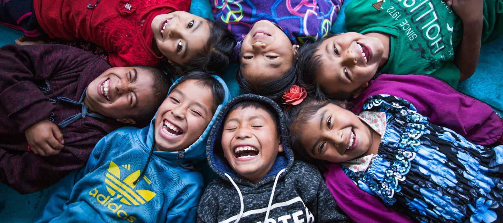Seven children, boys and girls, laying on their backs creating a circle, laughing.