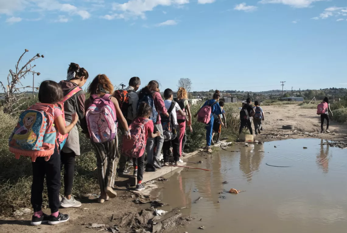 Roma children go to school amidst garbage and muddy water.