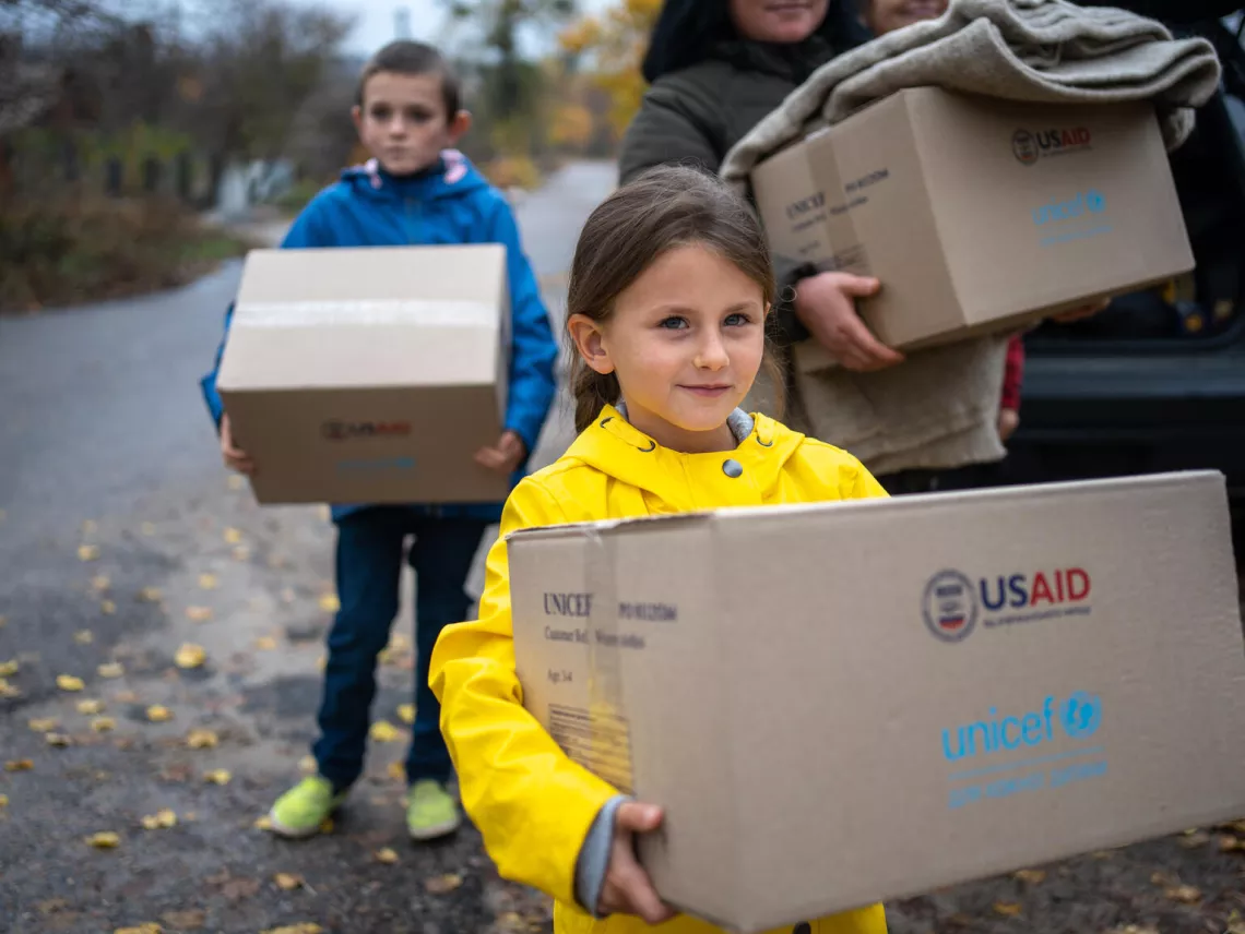 &Alpha; little girl carries a box of winter clothes, received from UNICEF. Her brother Sasha is behind her.