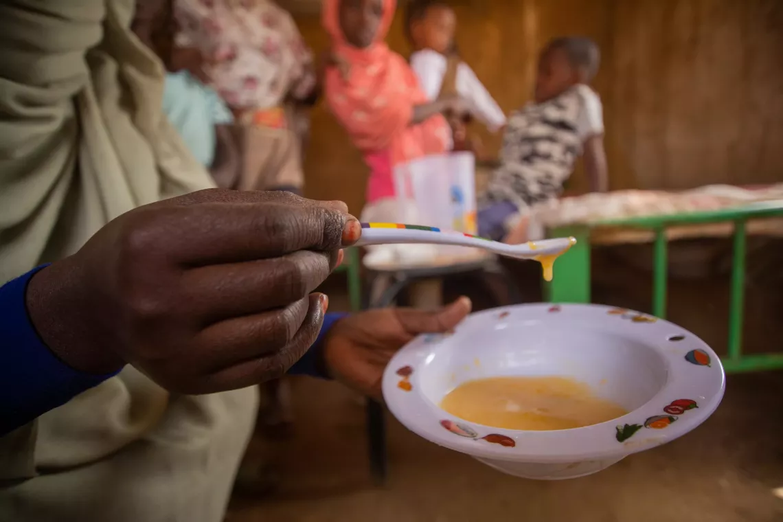  A mother of six children uses the special spoon provided with the complementary bowl, to measure the thickness of the meal she is about to serve her 9 months old son .