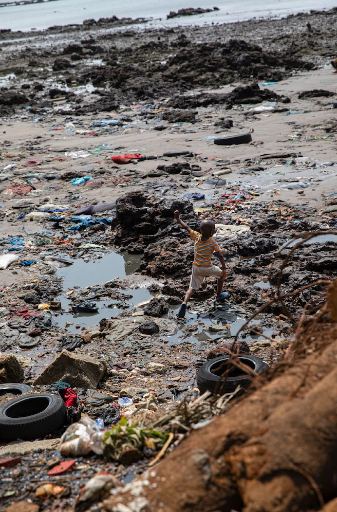 A child plays alone on the seashore among the garbage. Temenetaye artisanal fishing port, Conakry, Guinea.