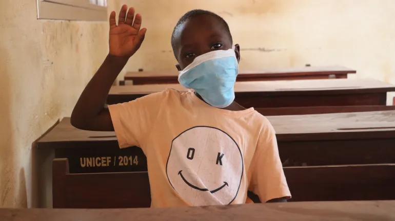 Child wearing a mask and raising hand in class room