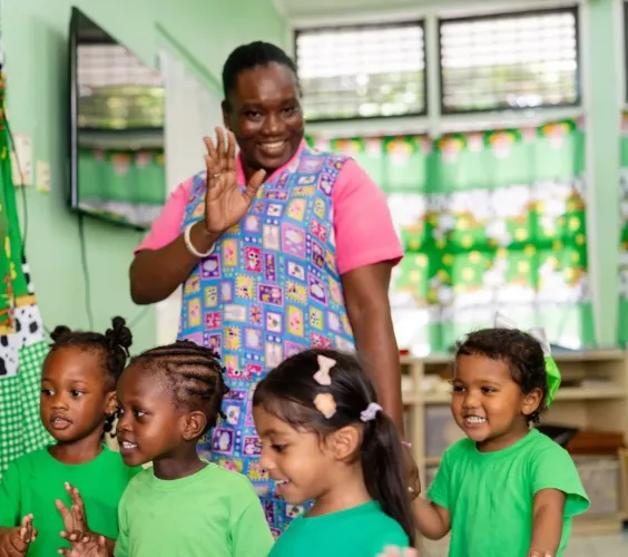 Teacher Samantha smiles and waves alongside a joyful group of children as they head to the playground