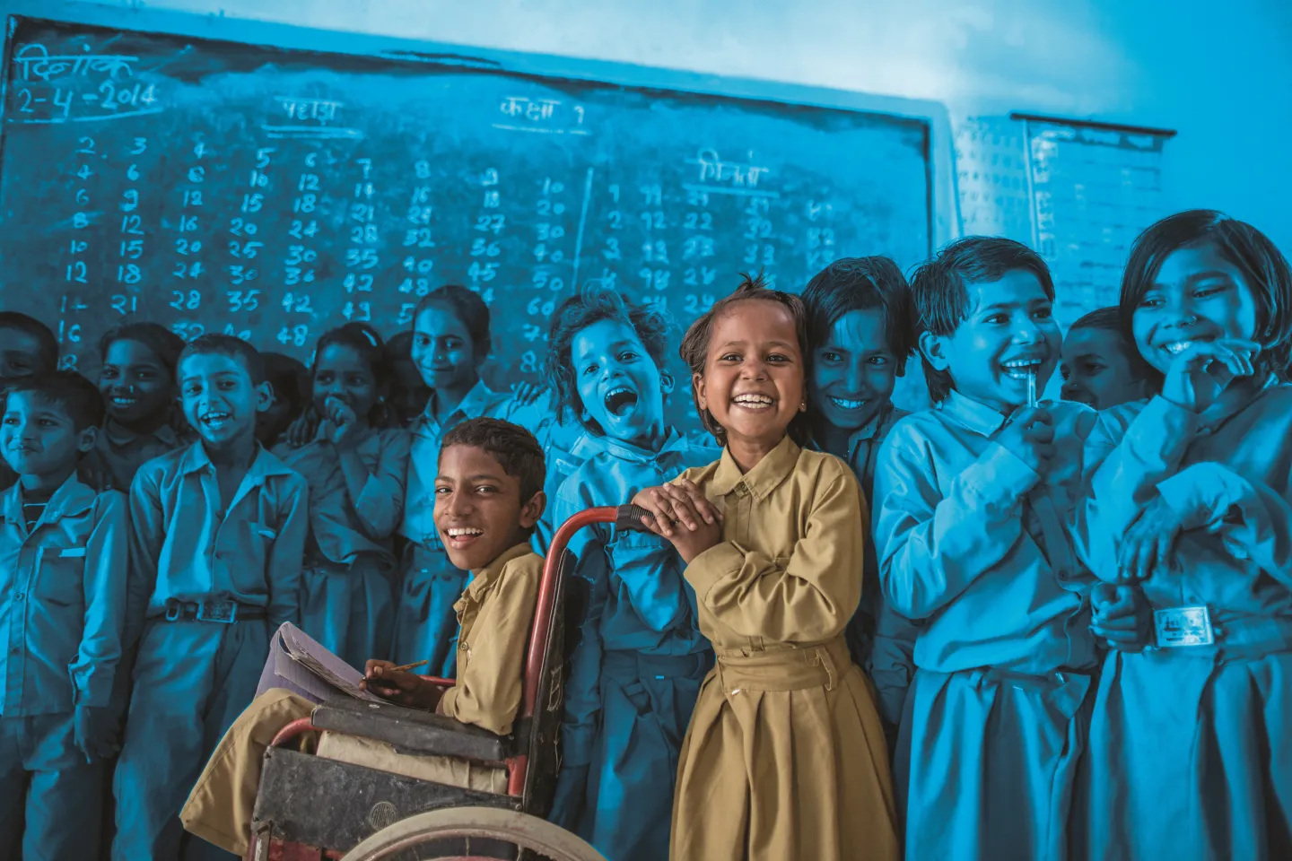 A joyful Indian schoolgirl in a khaki uniform laughs brightly beside a boy in a wheelchair, surrounded by smiling classmates in front of a blackboard a powerful image of inclusive education.