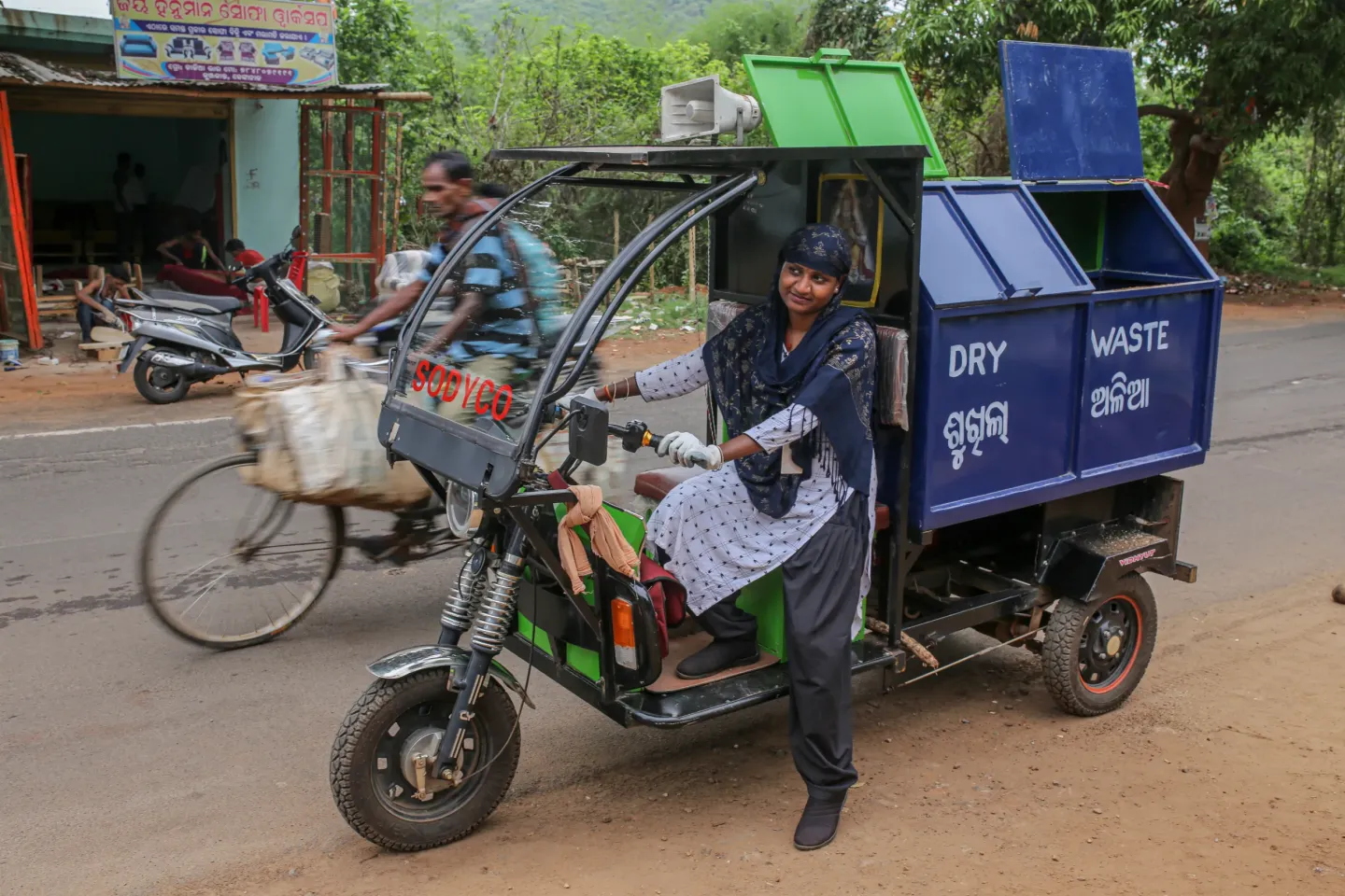A woman waste collection worker drives a "SODYCO" electric tricycle fitted with segregated dry and wet waste compartments in Odisha &mdash; part of a women-driven solid waste management initiative supporting clean communities and women's livelihoods.