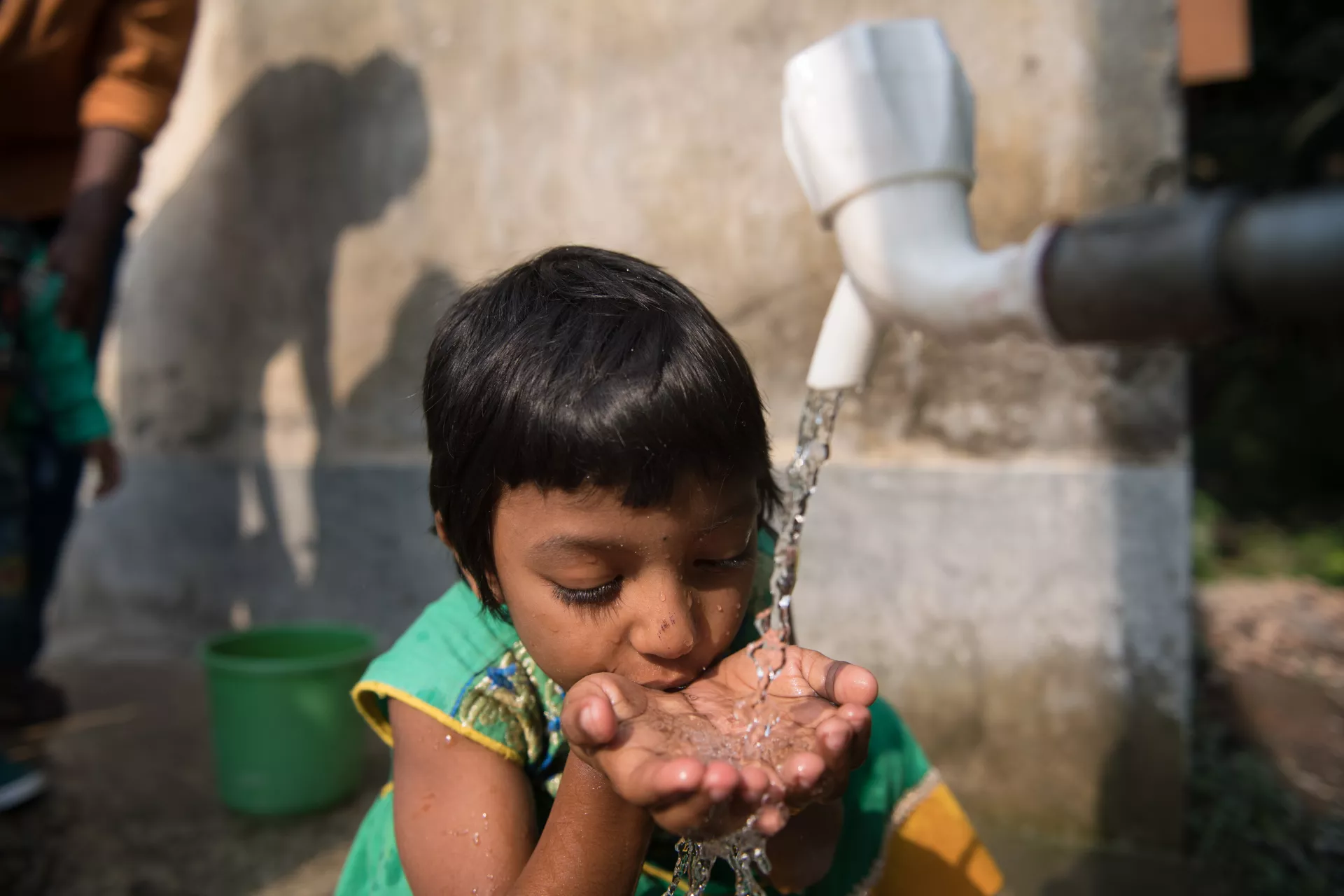 A girl cups her hands under a tap and drinks clean water