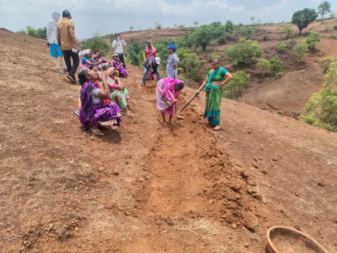 A group of rural women in colourful sarees dig and hoe a Continuous Contour Trench on a dry red-soil hillside in Maharashtra during a community Shramdaan water conservation campaign.