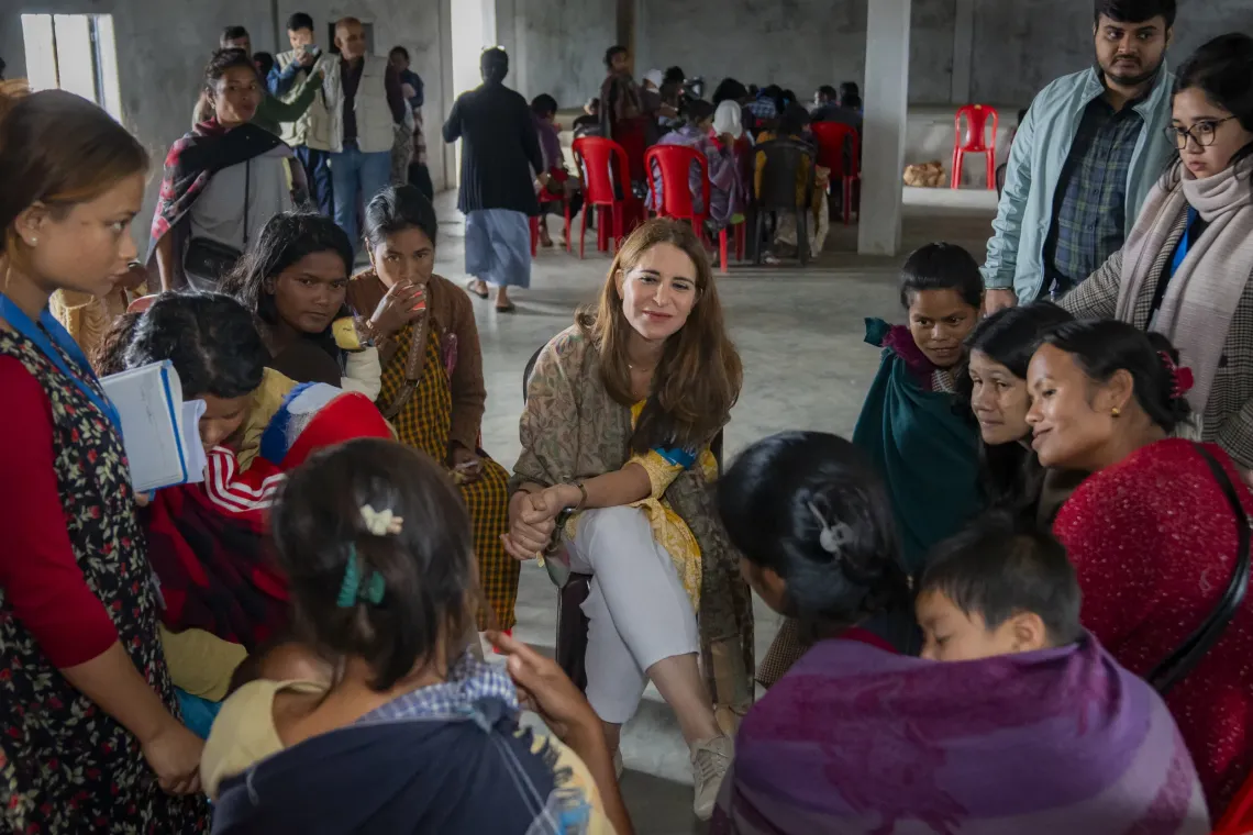 UNICEF India's Chief of Field Services sits among a group of women and children gathered in a community hall in rural Meghalaya, listening attentively as part of a women-led discussion on immunization, with red chairs and other community members visible in the background.