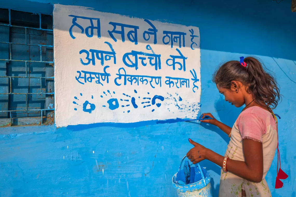 A girl paints on a wall using blue paint.