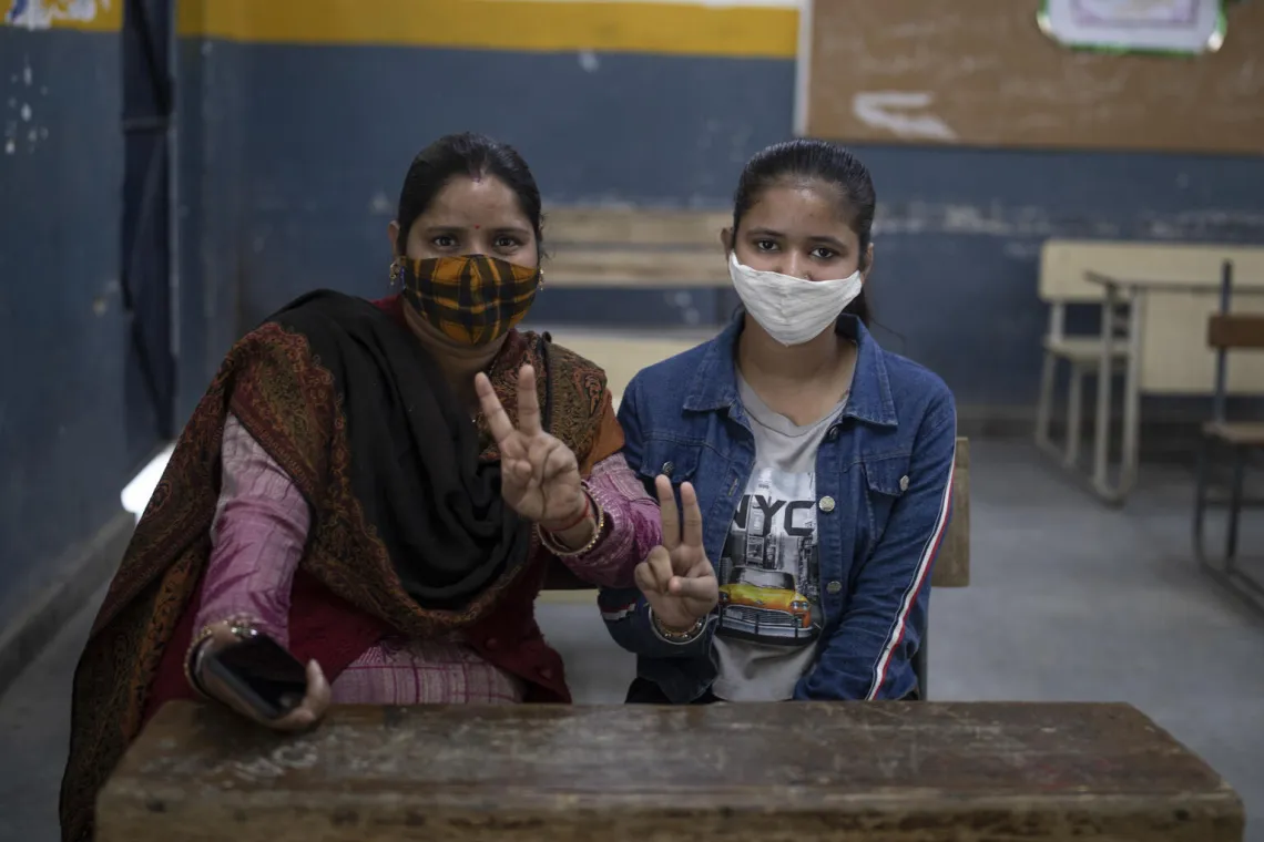 Shruti, 14, and her mother Rajni, flashes a victory sign after receiving a vaccination dose for COVID-19 at a vaccination center in New Delhi,
