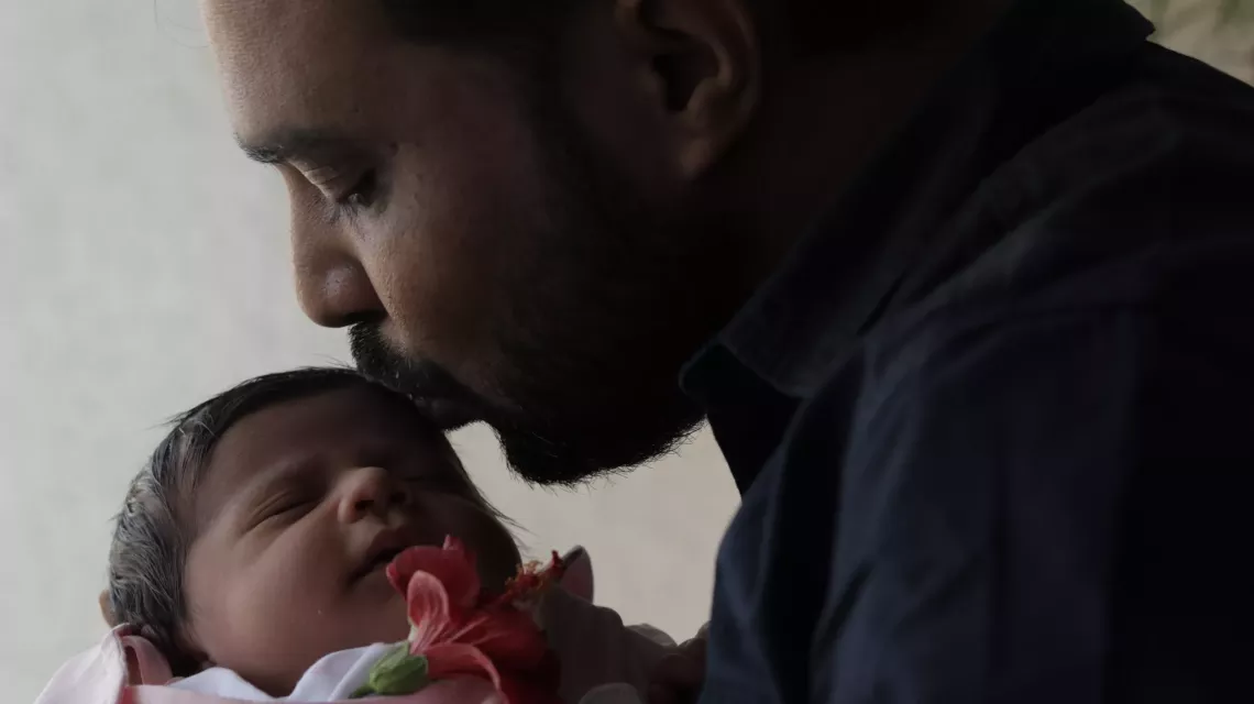 Ashish, kissing his newborn daughter&rsquo;s forehead