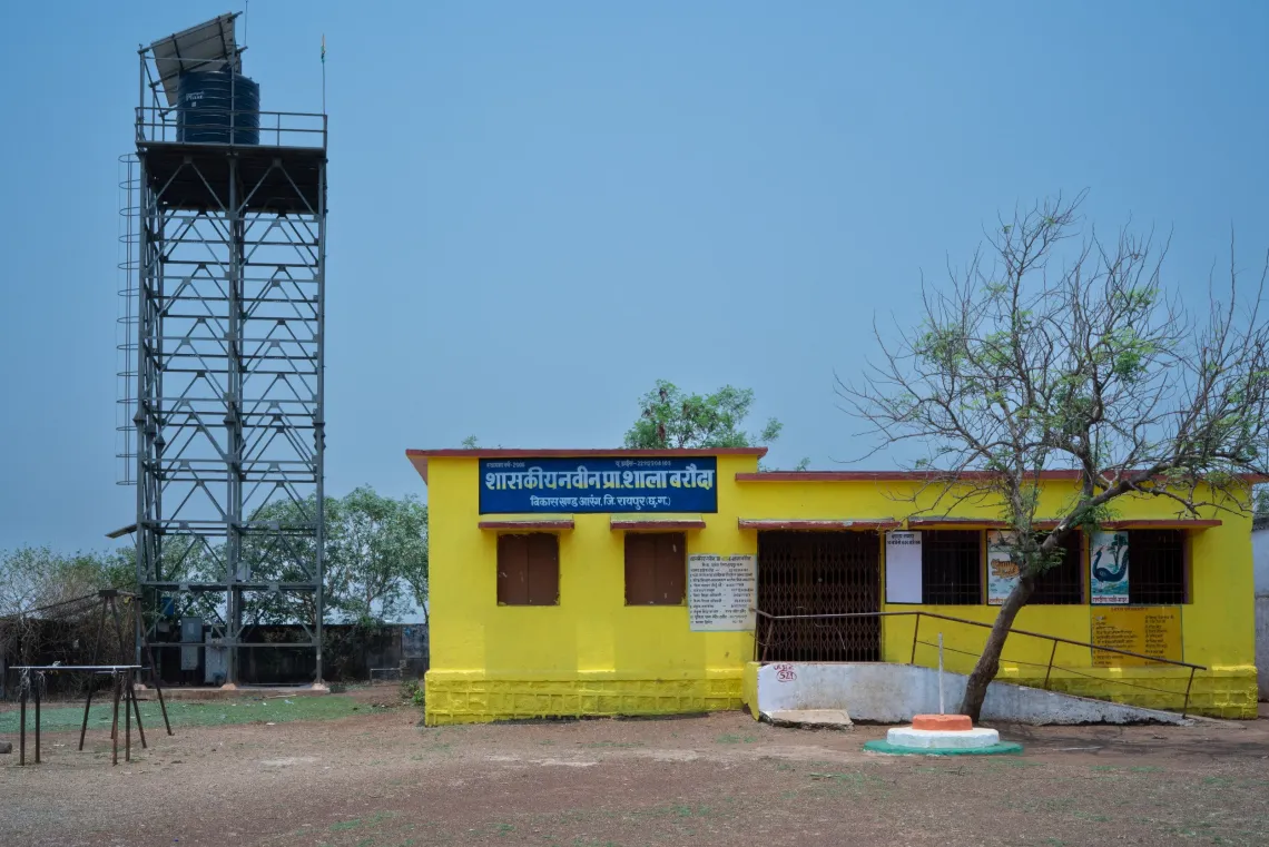Small yellow building with blue sign, next to metal watchtower and tree under clear sky.