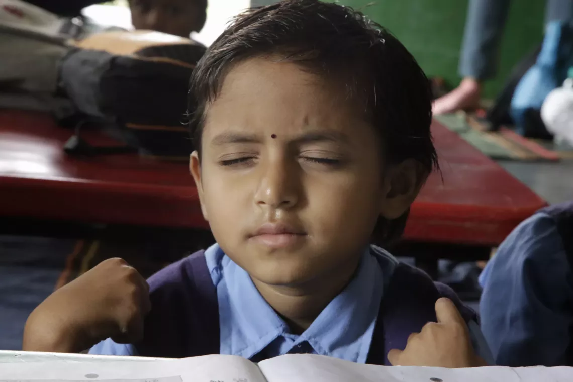 A child in school uniform sitting at a desk in class with their eyes shut thinking.