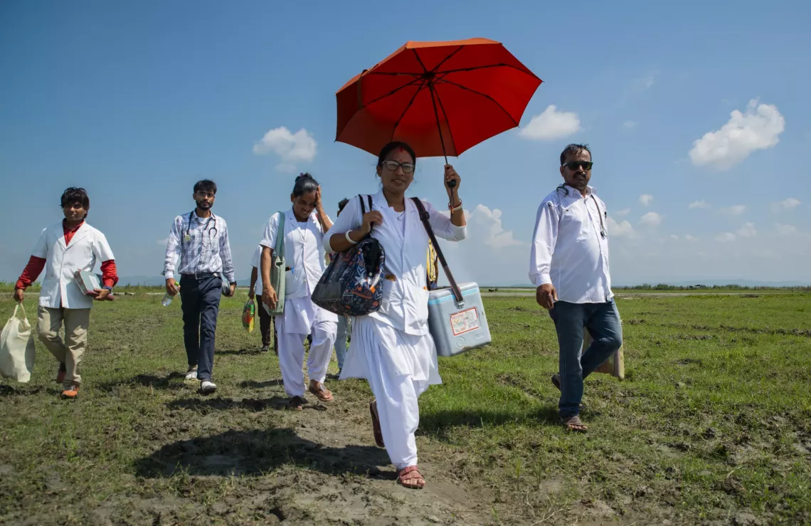 Nirupoma Roy and her colleagues walk over a kilometre and a half to a makeshift health centre, carrying medicines and equipment to provide services.