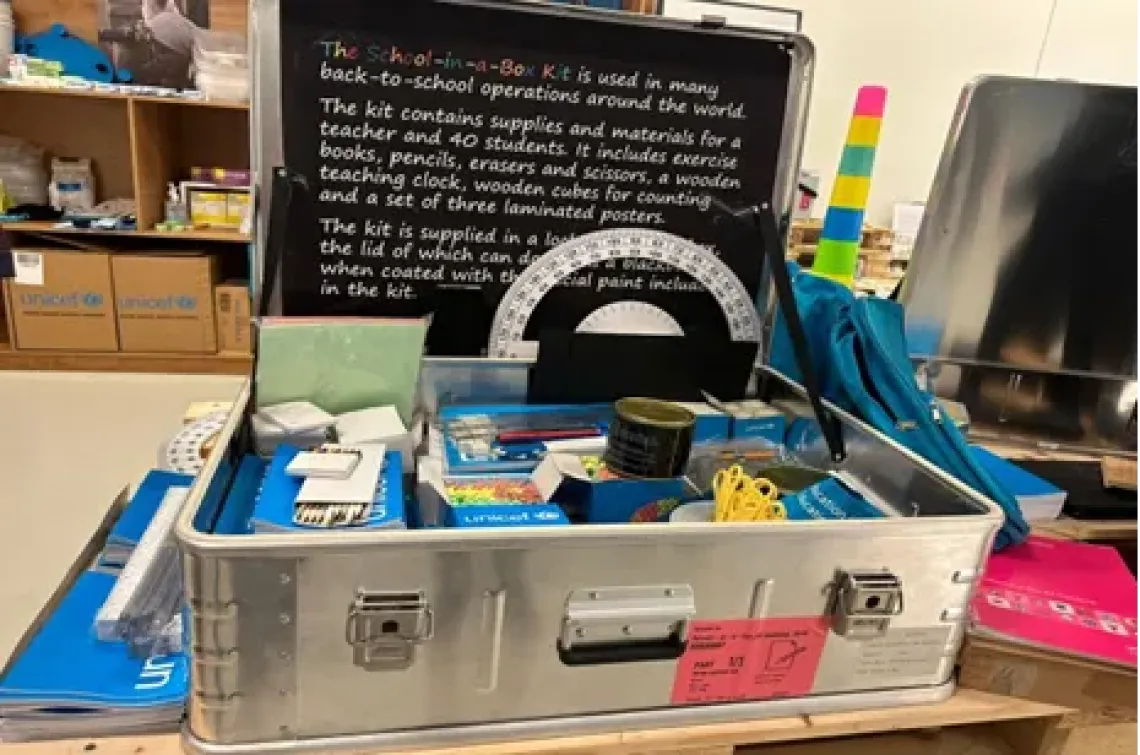 An open UNICEF School-in-a-Box aluminium kit filled with educational supplies for a teacher and 40 students, with a description label inside the lid.