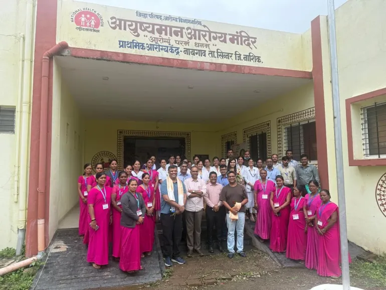 ASHA workers in pink saris, health staff and visitors pose outside the Primary Health Centre in Naygaon, Nashik