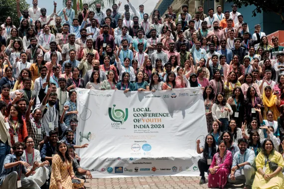A large group of young climate leaders pose together on an outdoor stairway, holding a banner for the Local Conference of Youth (LCOY) India 2024 in Mysuru, Karnataka.