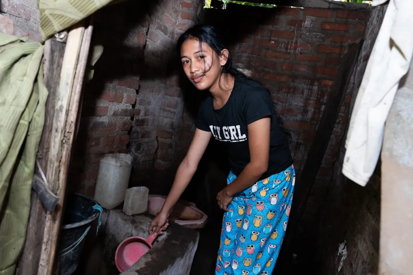 A girl uses a water scooper in the bathroom in her house