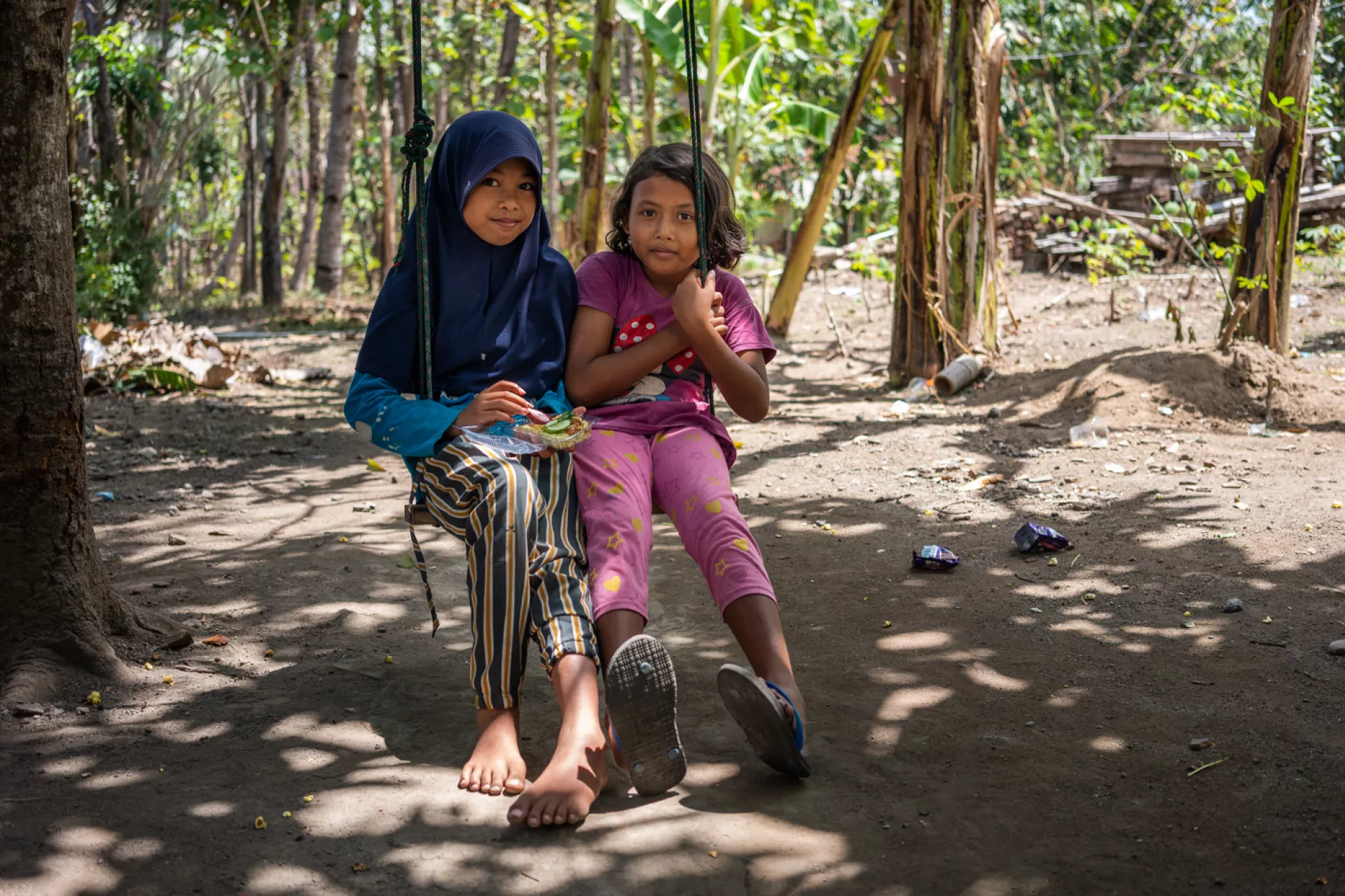 Two girls eat as they sit together on a swing outside their home in Central Java province, Indonesia.