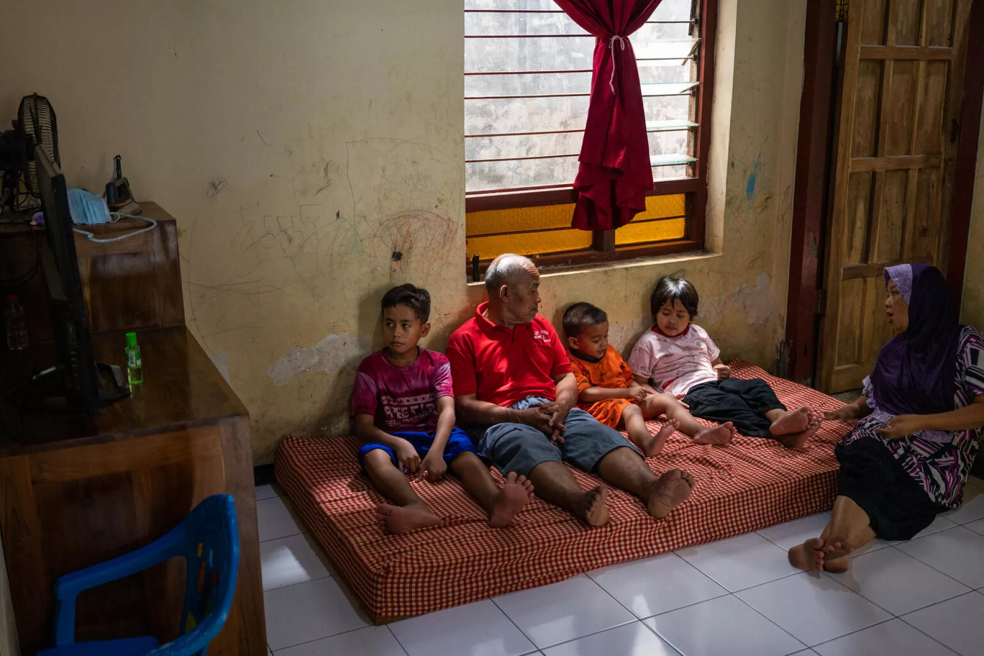 Faishal and his brothers watch TV with their grandparents at home.