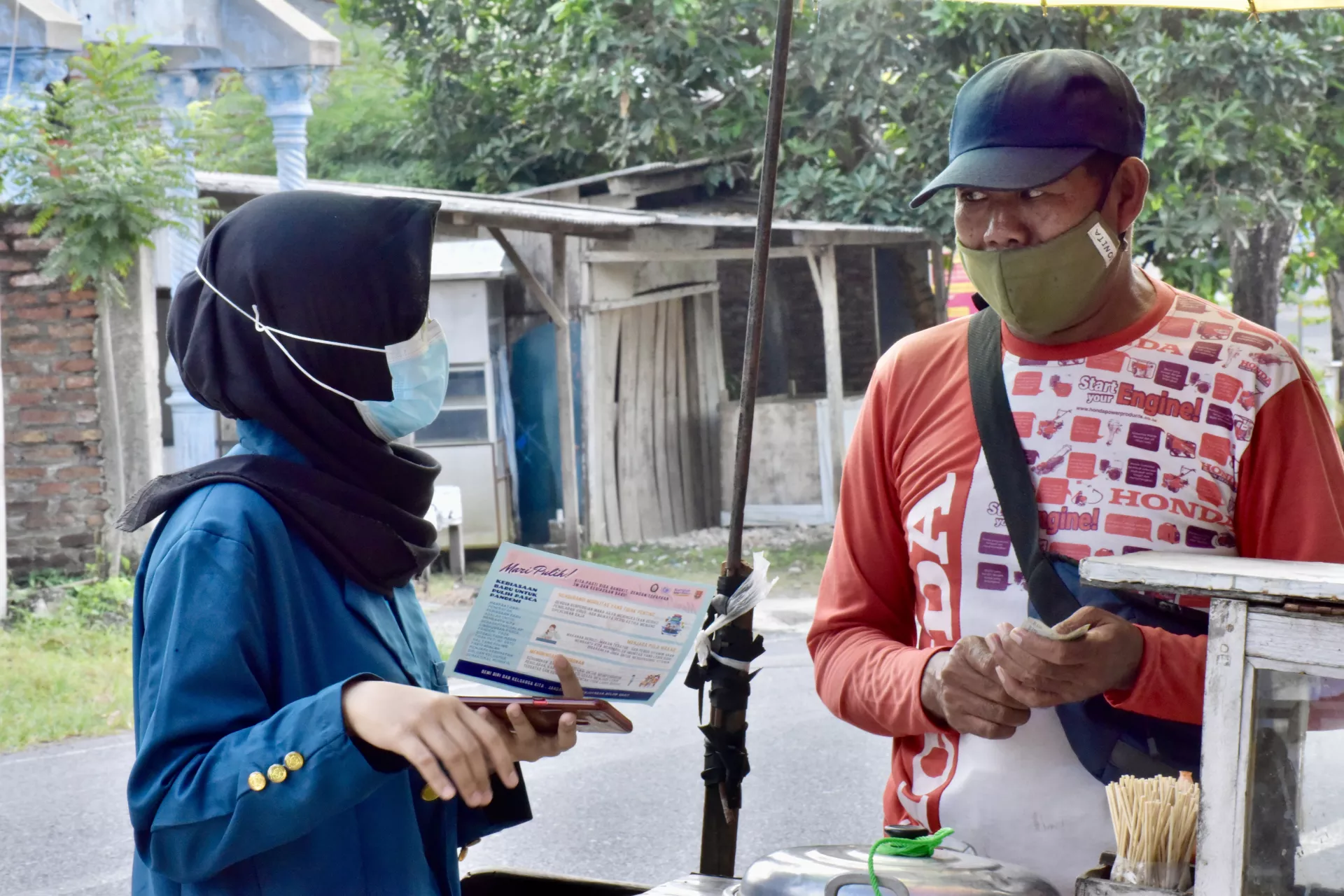 Megawati Sekar nampak sedang mendekati penjual asongan untuk membagikan selebaran berisi informasi 3M-mencuci tangan, menjaga jarak dan mengenakan masker. 