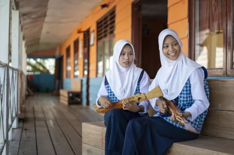 Two schoolgirls playing the Oku Lele musical instrument at their school.